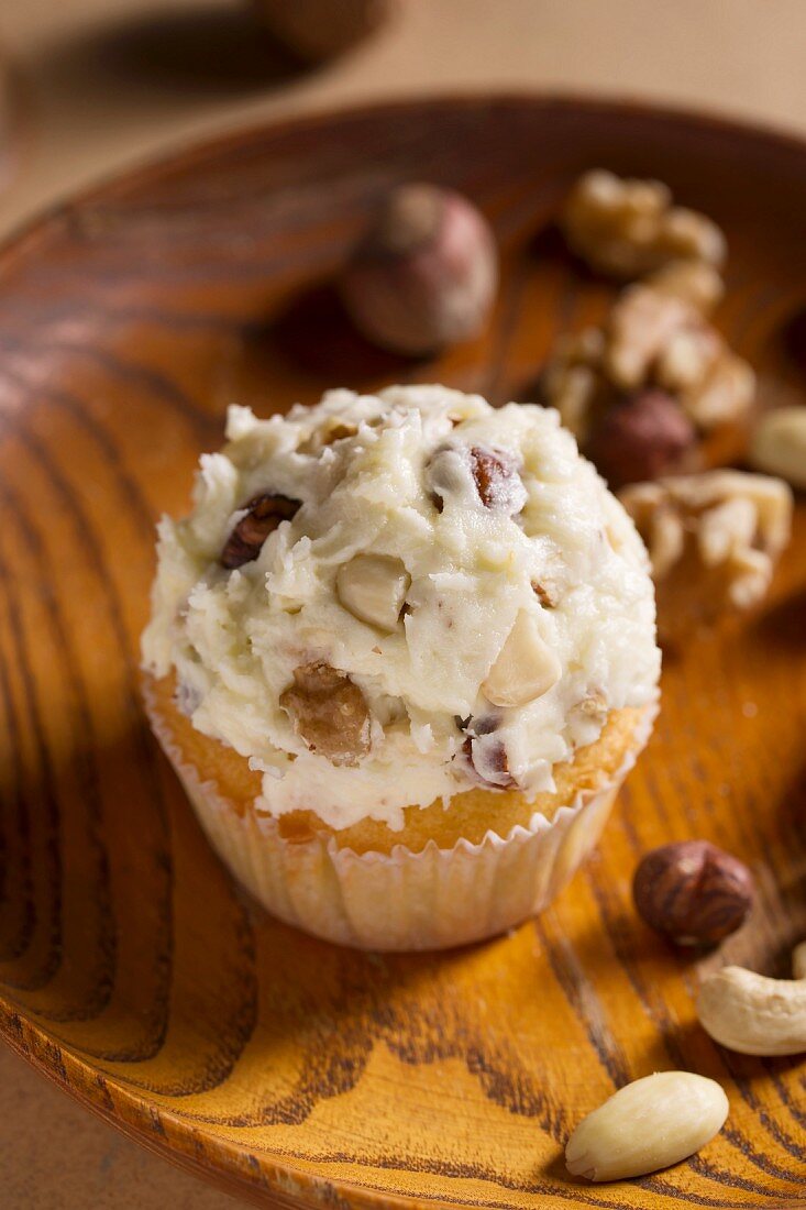 Cupcake with nuts in the icing, on a wooden plate
