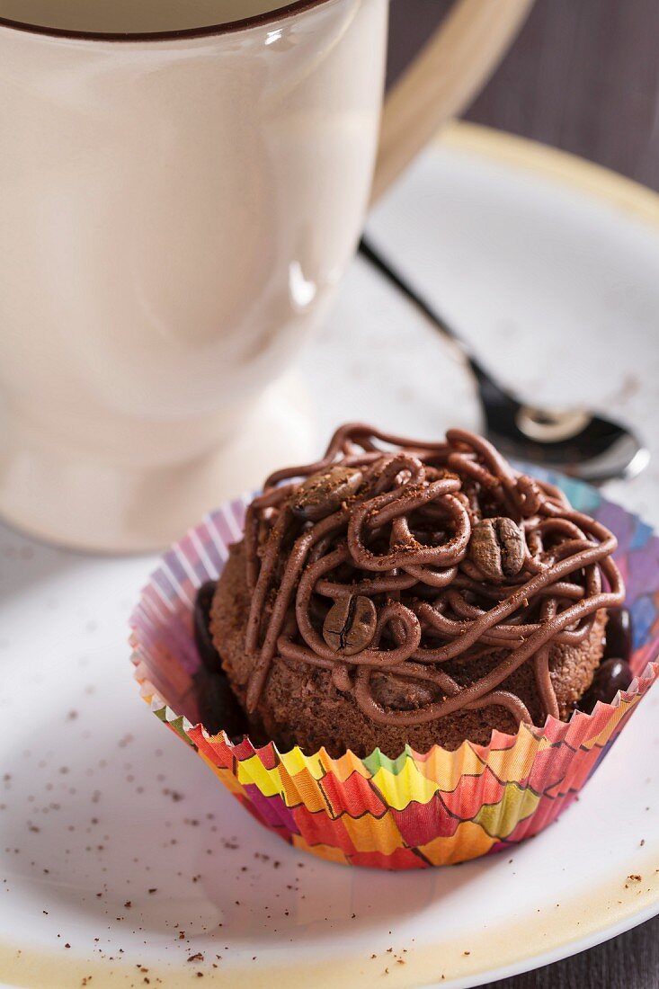 A mocha cupcake with coffee beans, a cup of coffee