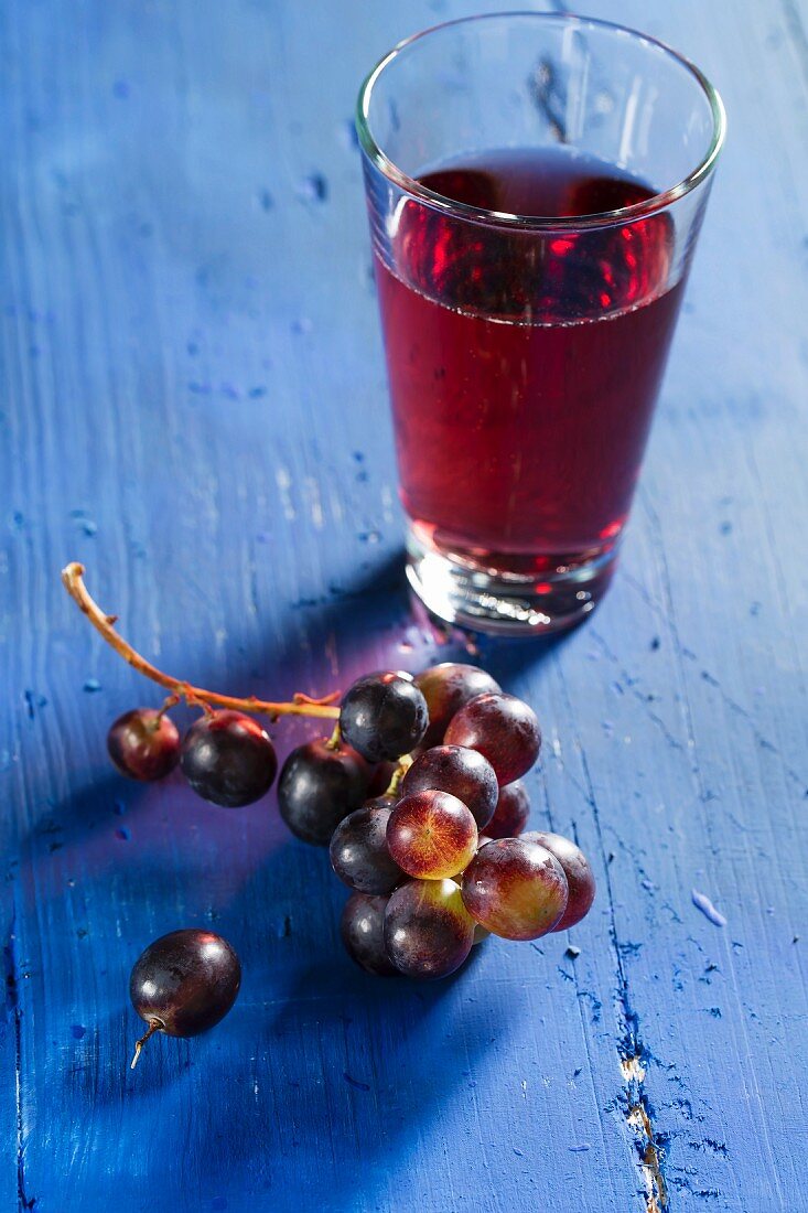 Rote Weintrauben und Traubensaft auf blauem Holzbrett