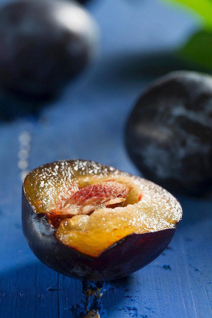 Plums, one halved, on a blue wooden tabletop
