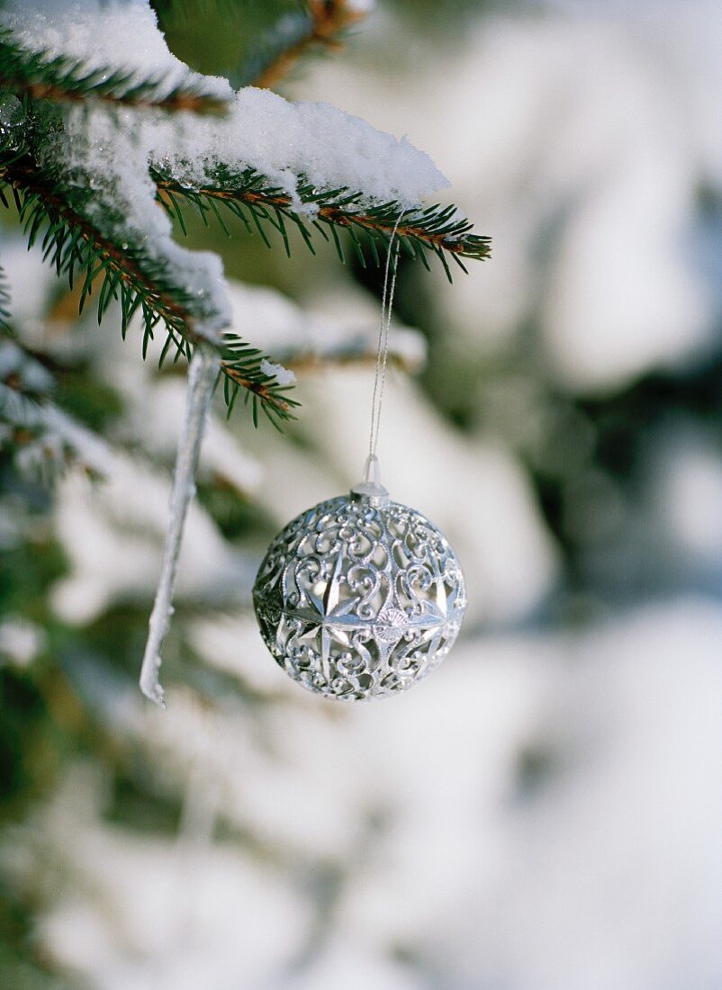 Silver bauble hanging from snow-covered fir branch