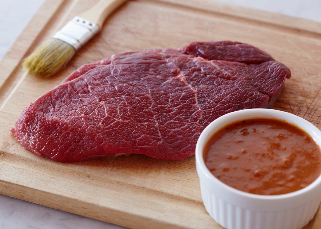 Rohes Rindfleisch auf Schneidebrett mit einem Schälchen Marinade