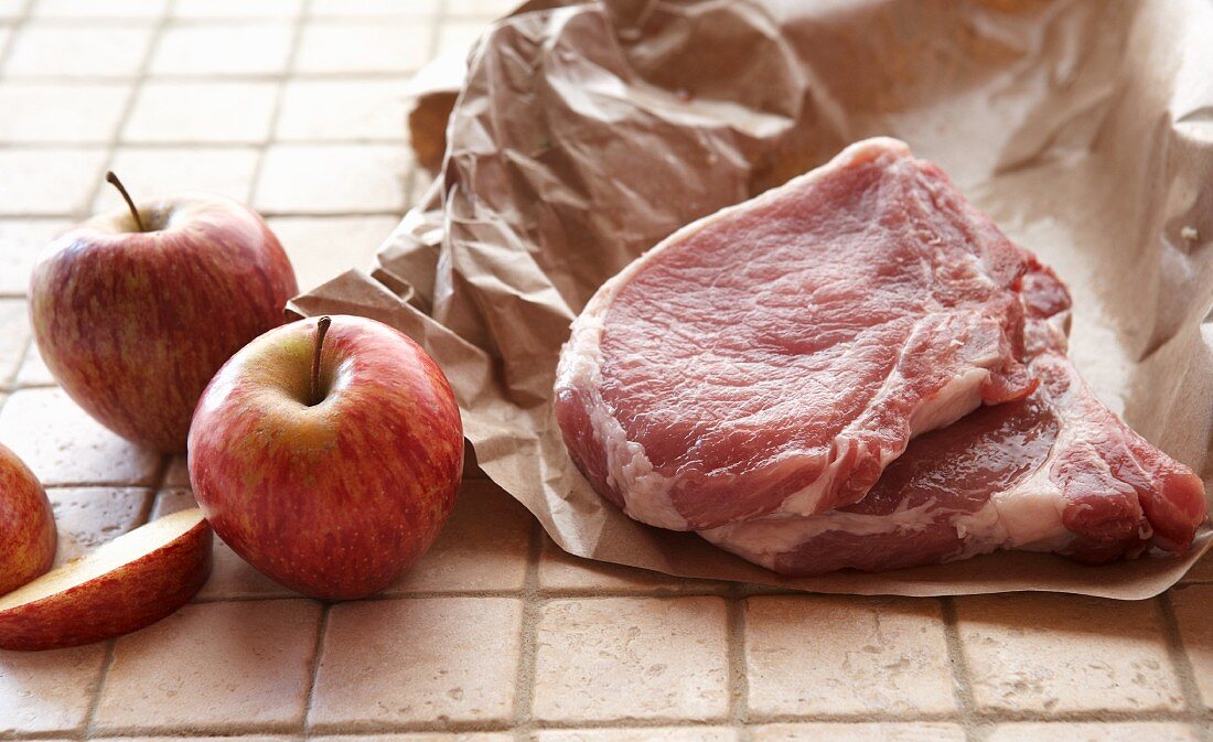 Schweinekoteletts auf Papier, daneben rote Äpfel