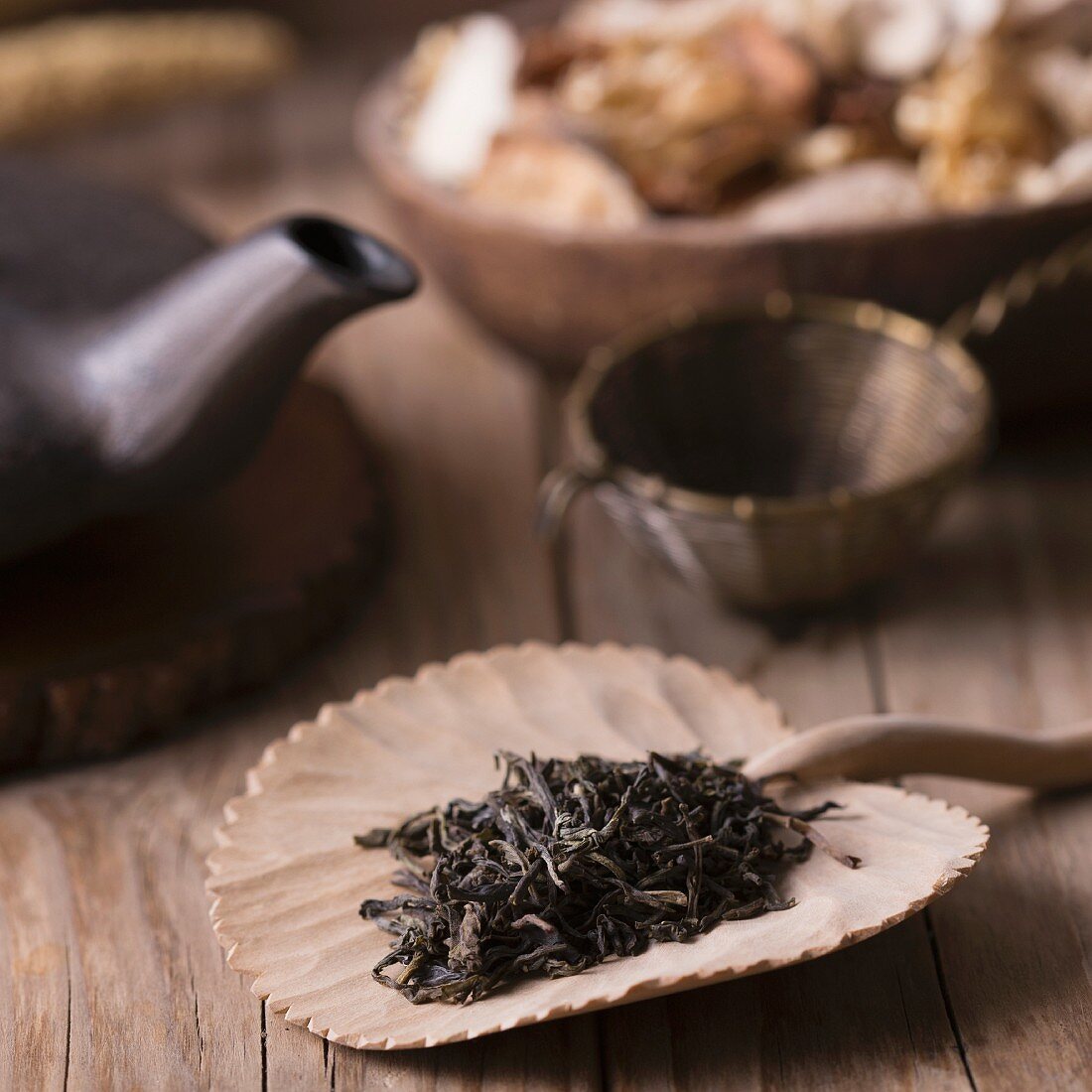 Spoon of dried green tea leaves on wooden background