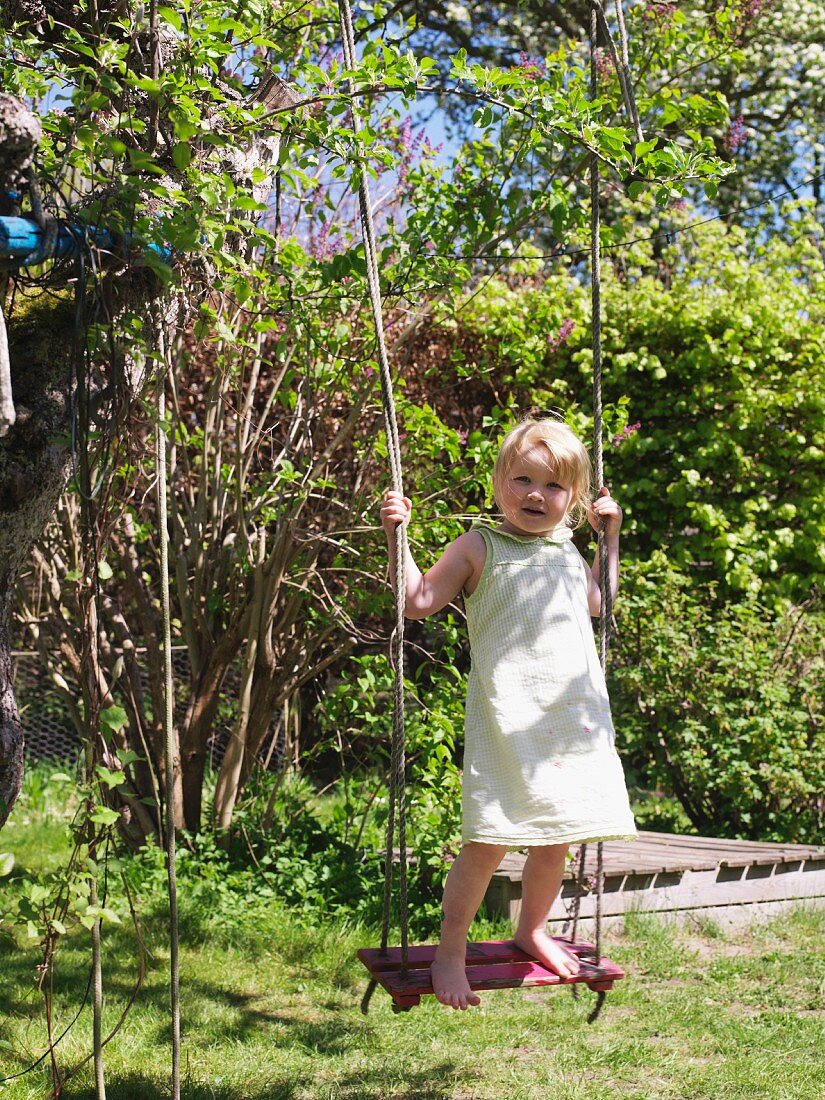 Little girl standing on swing in garden