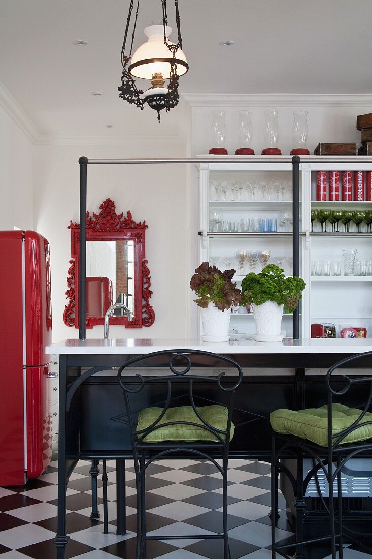 Bar stools with wrought iron and green seat cushions in front of breakfast bar; mirror with red, ornate frame and white, glass-fronted cabinet in background