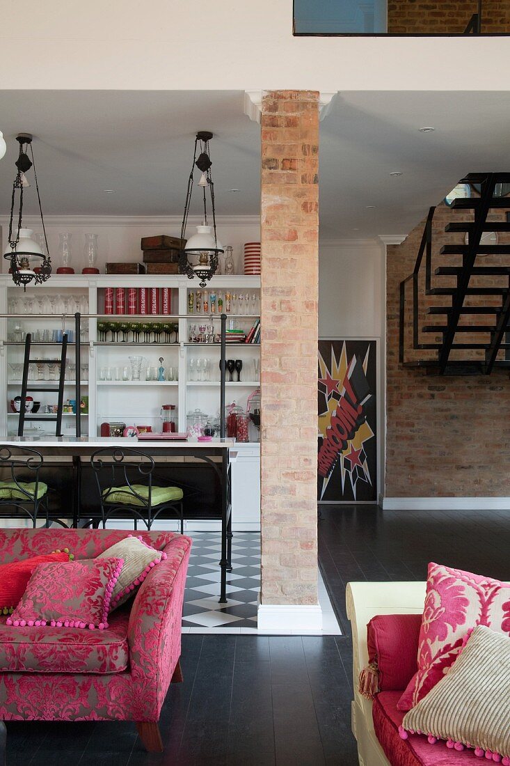 Brick pillar in front of kitchen area, elegant seating in foreground and staircase against brick wall in open-plan interior