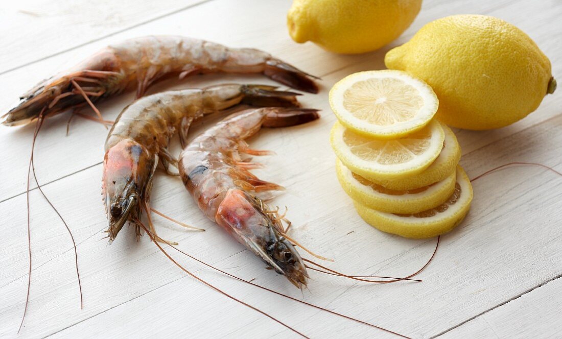 Three Raw Prawns next to Slices of Lemon