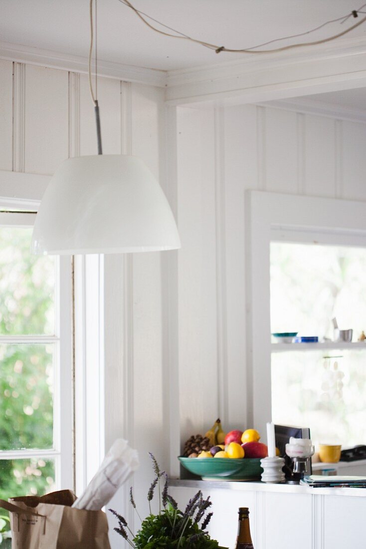 A Bright White Kitchen with a Brown Paper Grocery Bag on the Table and a Bowl of Fresh Fruit in the Background