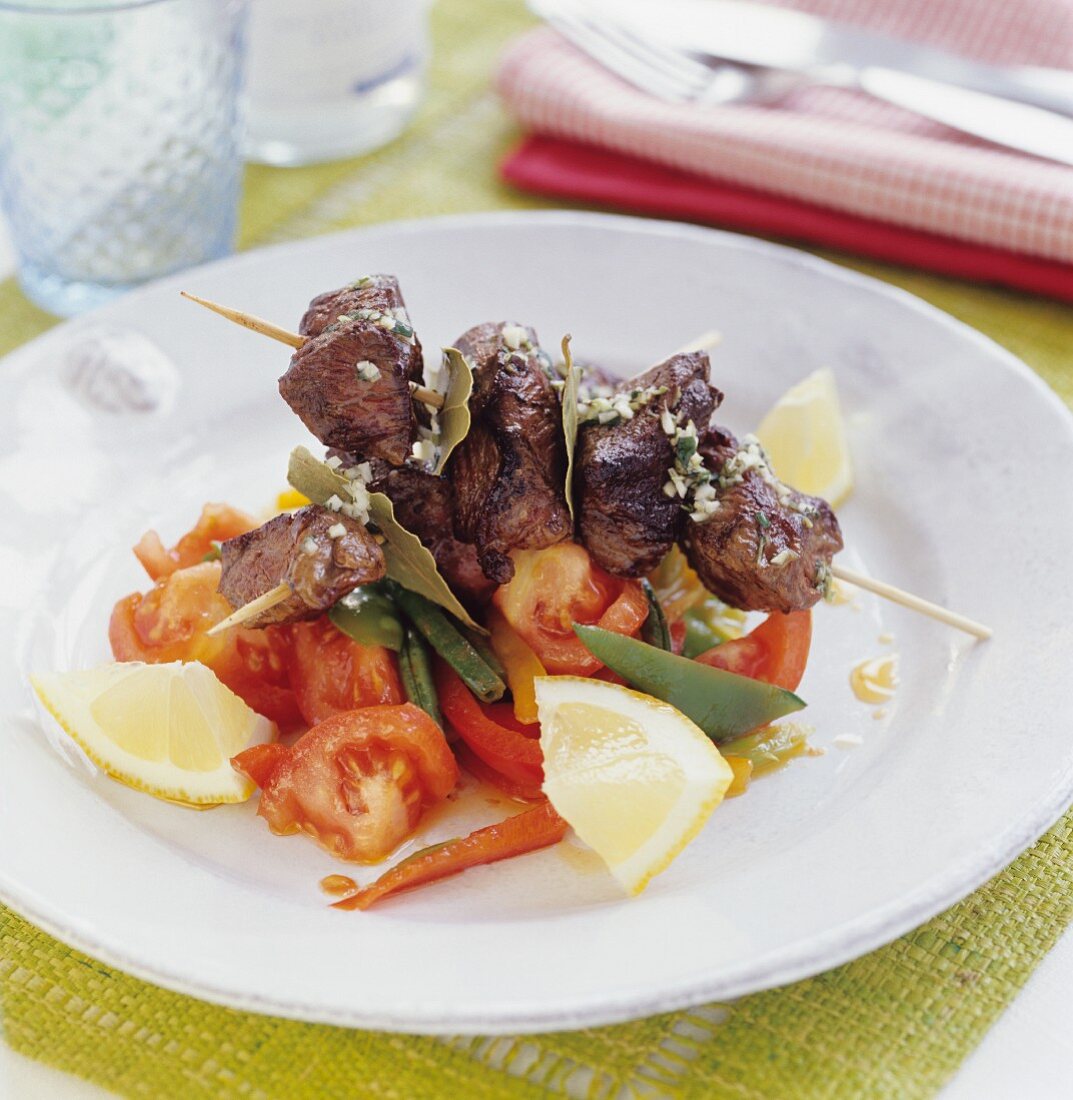 A skewer of lamb on tomato salad with lemons