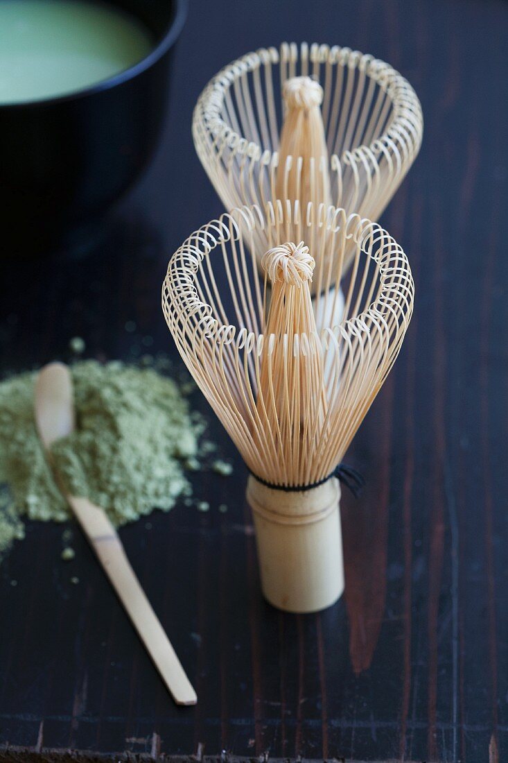 Two bamboo tea whisks, a matcha spoon and green tea powder
