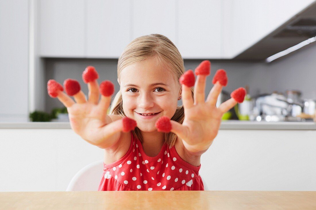 Mädchen zeigt ihre Hände mit Himbeeren auf den Fingerspitzen