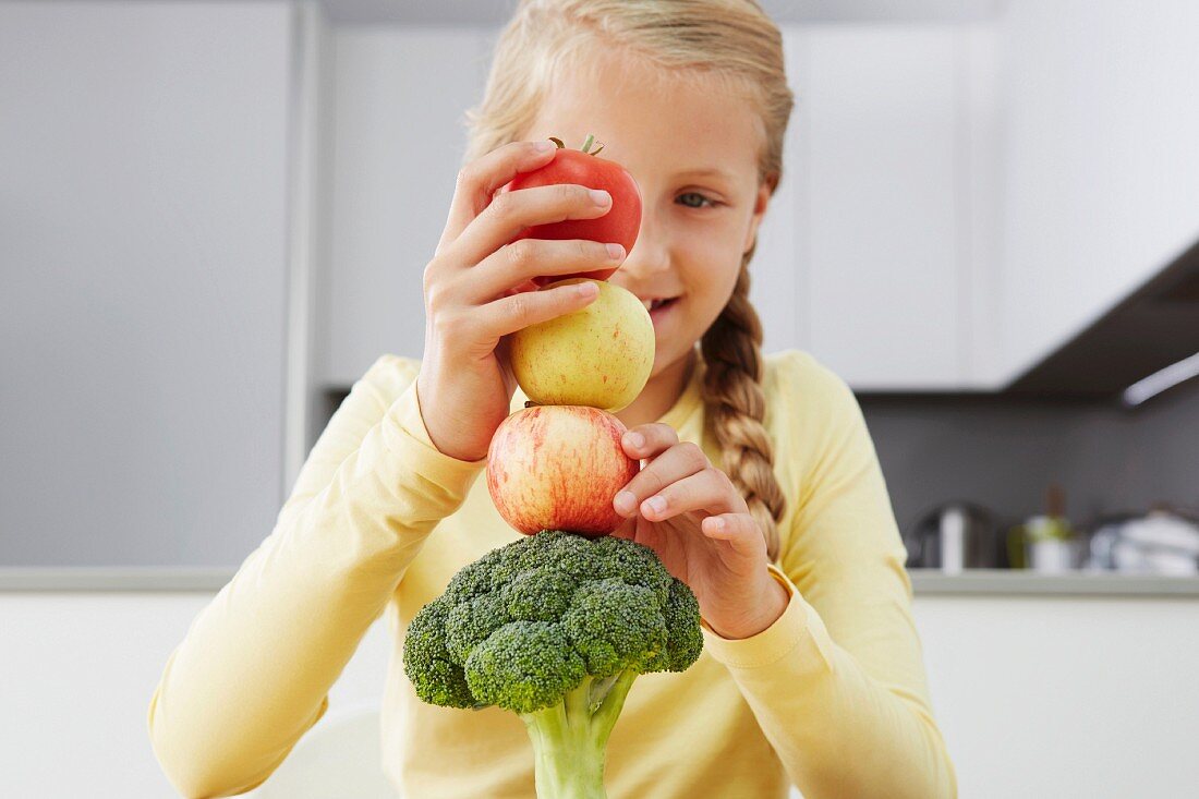 Mädchen baut einen Turm aus Gemüse und Äpfeln