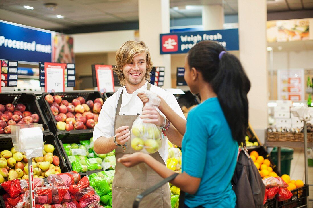 Junger Verkäufer reicht Kundin Äpfel in Plastiktüte im Supermarkt