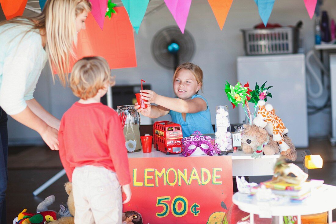 Mädchen verkauft der Mutter Limonade an einem Spiel-Verkaufsstand