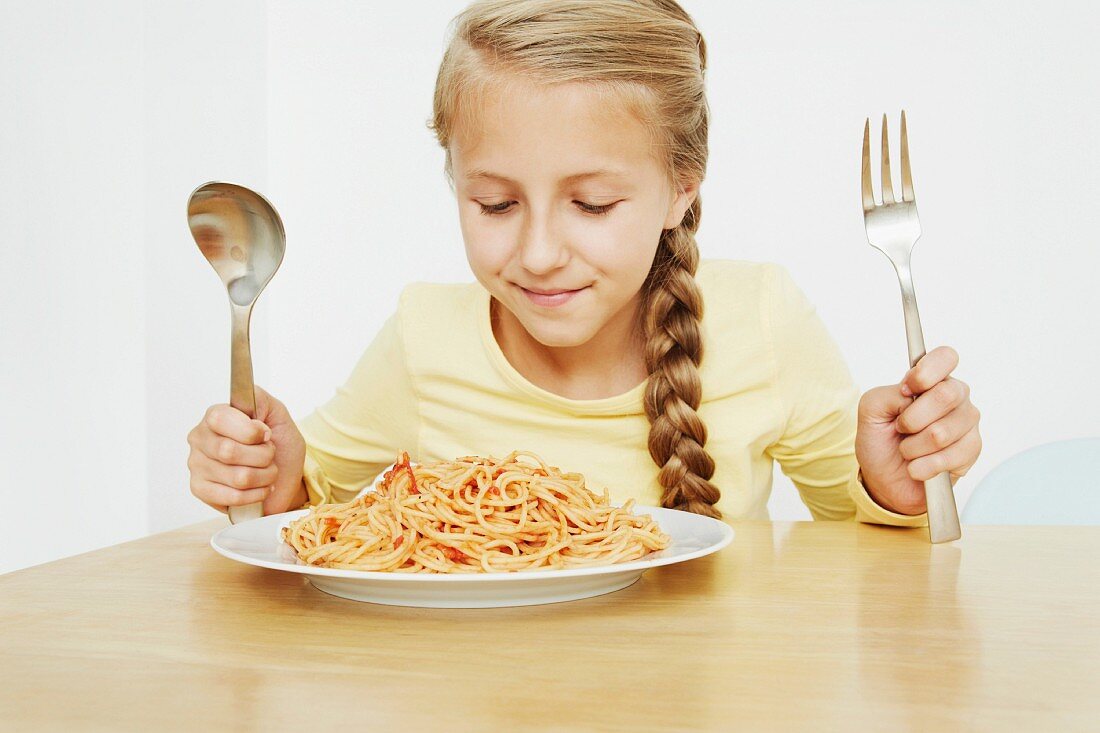 Mädchen mit einem Teller Spaghetti und übergrossem Besteck