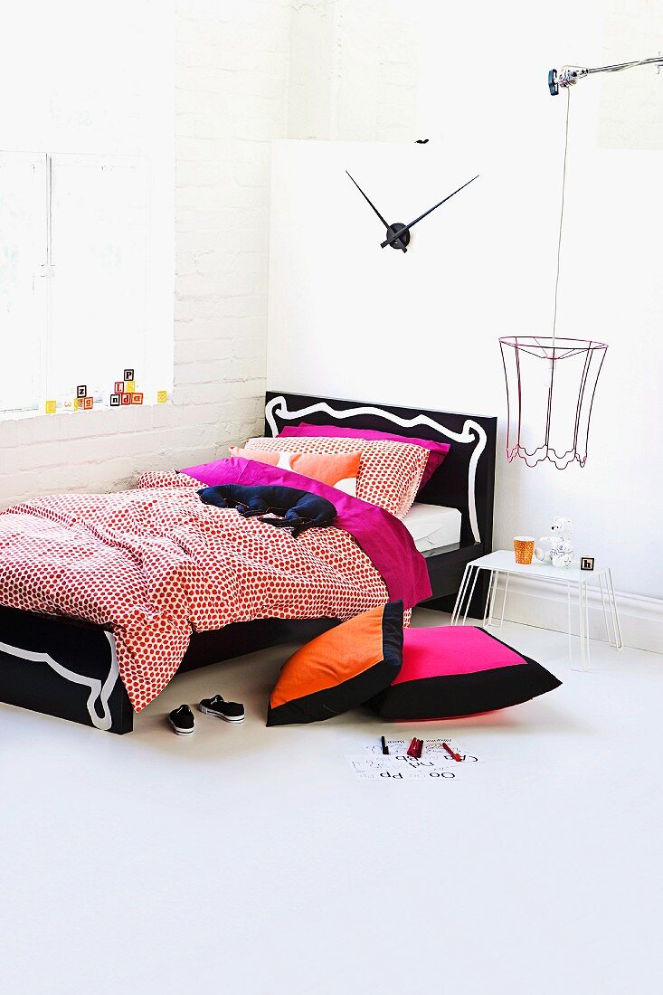 Colourful bed linen and soft toy on wooden bed with ornate headboard and wire lampshade in teenager's bedroom