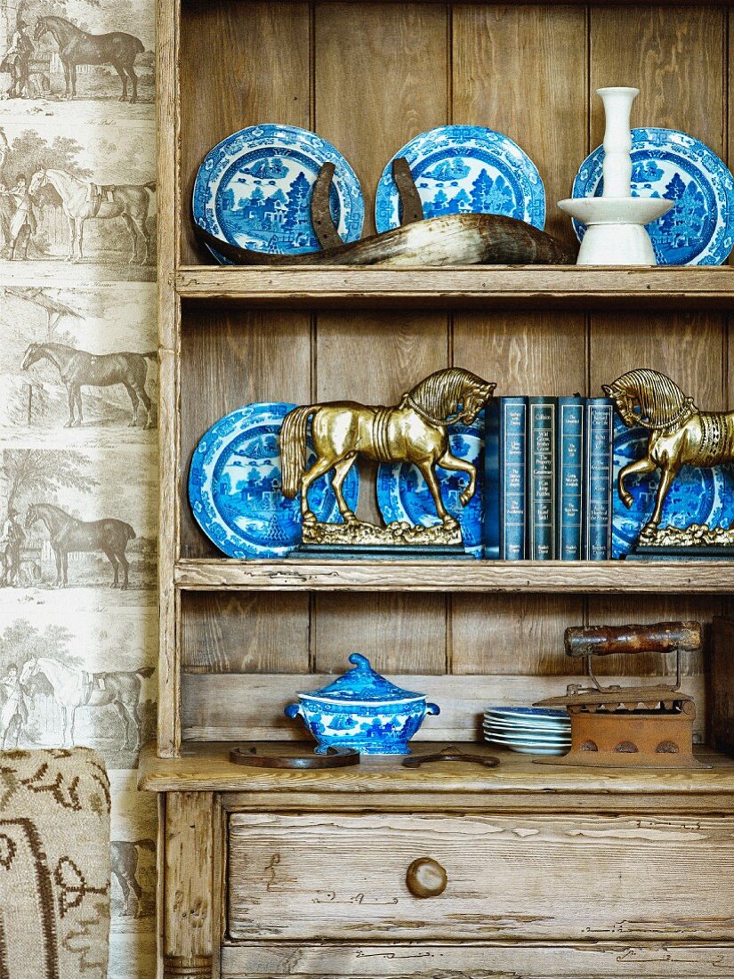 Small, brass horses in front of blue and white plates on shelves of rustic wooden dresser