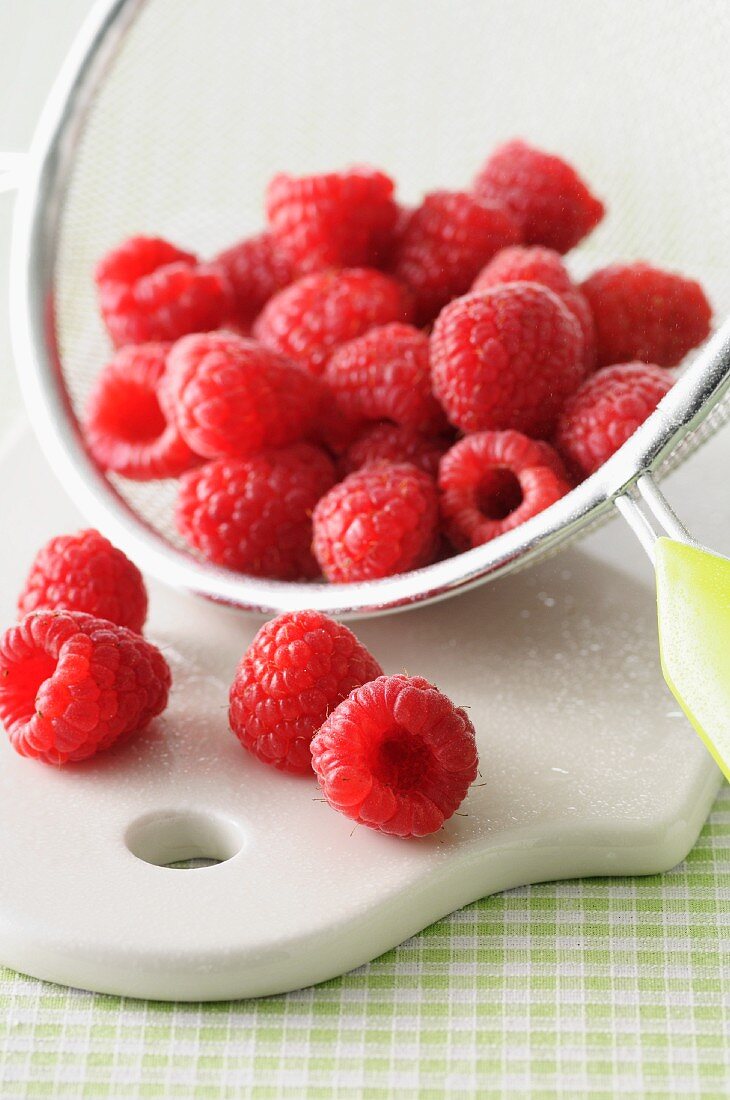 Frische Himbeeren im Sieb auf Schneidebrett