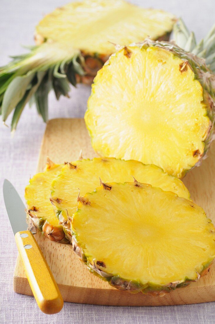 Pineapple, in slices and cut in half, on a chopping board