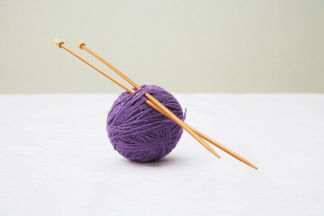 Ein violettes Wollknäuel mit Stricknadeln