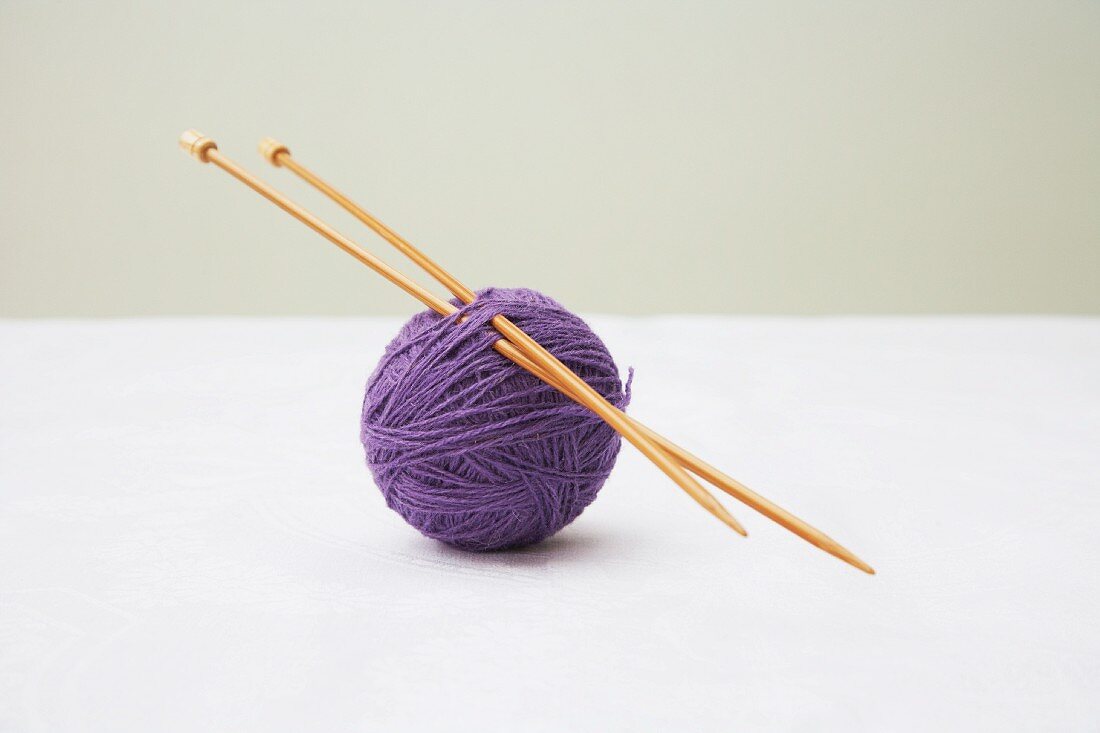 Knitting needles stuck through ball of purple wool