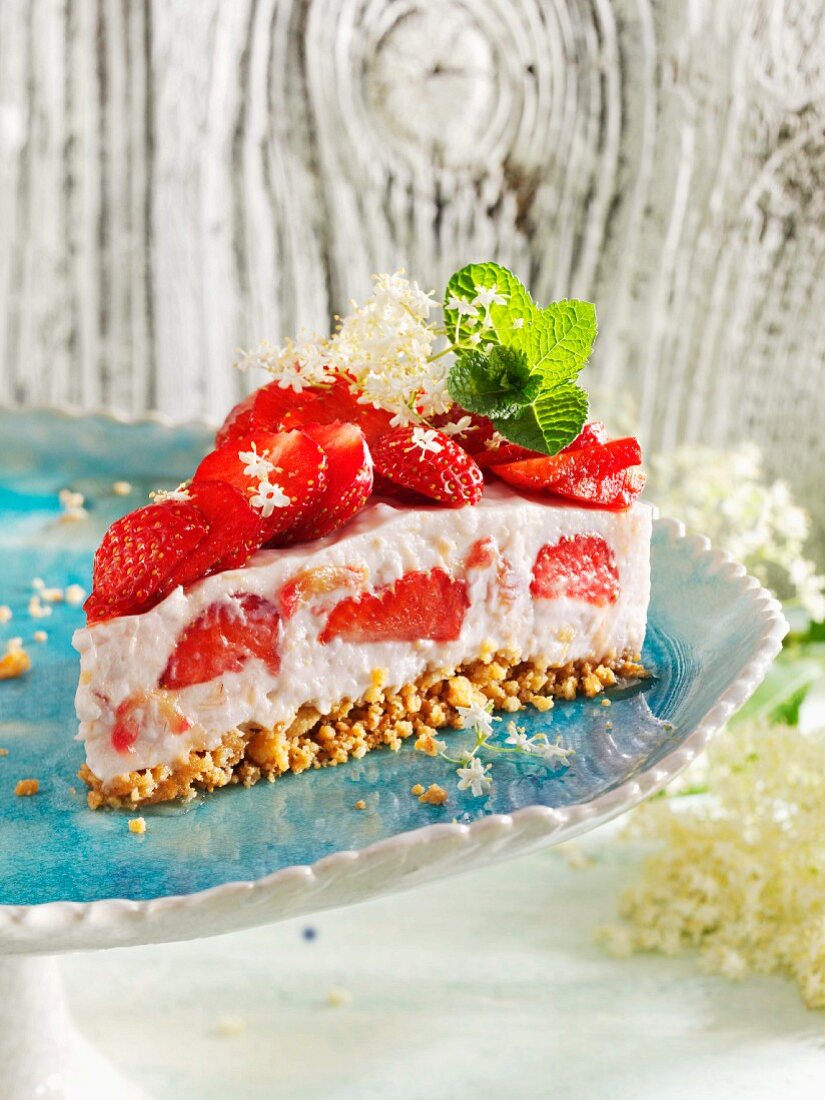 Ein Stück Rhabarber-Milchreis-Torte mit Erdbeeren und Holunderblüten