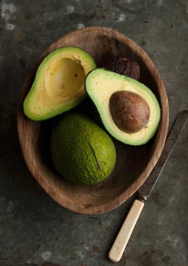Avocados, whole and cut in half, in a wooden bowl
