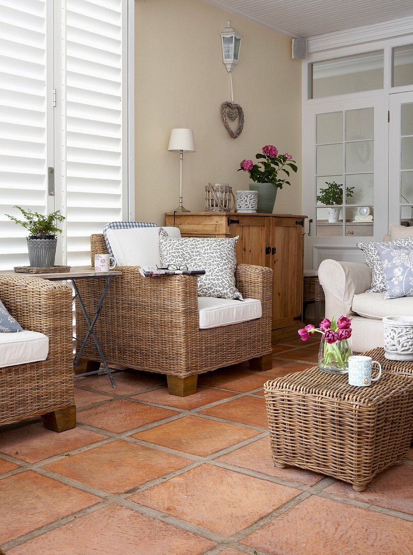 Wicker armchairs and stool on terracotta tiled floor in romantic, country-house interior