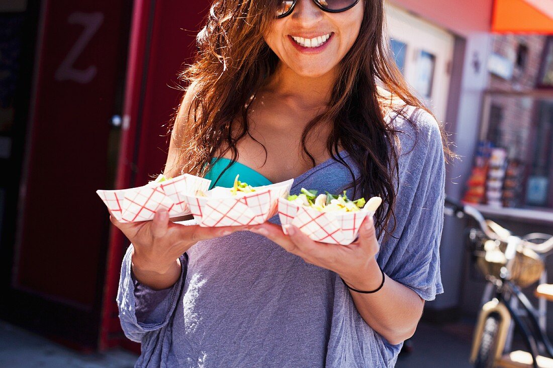 Lachende, sommerlich gekleidete Frau mit Fastfood in drei Pappschalen