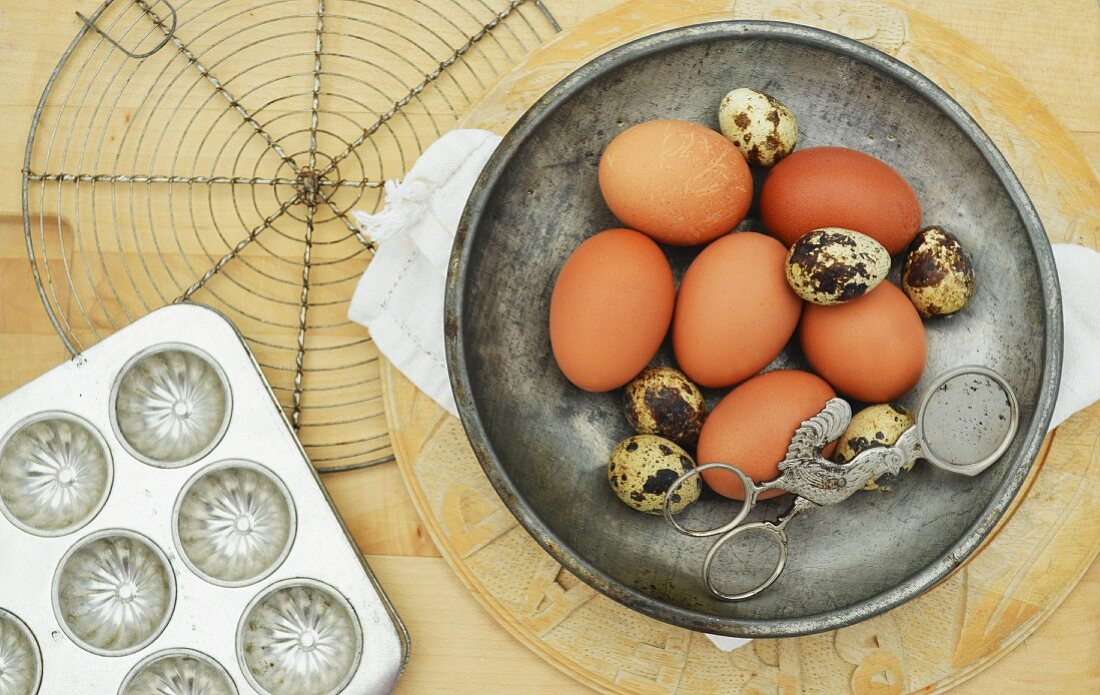 qualis and chicken eggs in a metal bowl with vintage baking equipment on a wooden chopping board