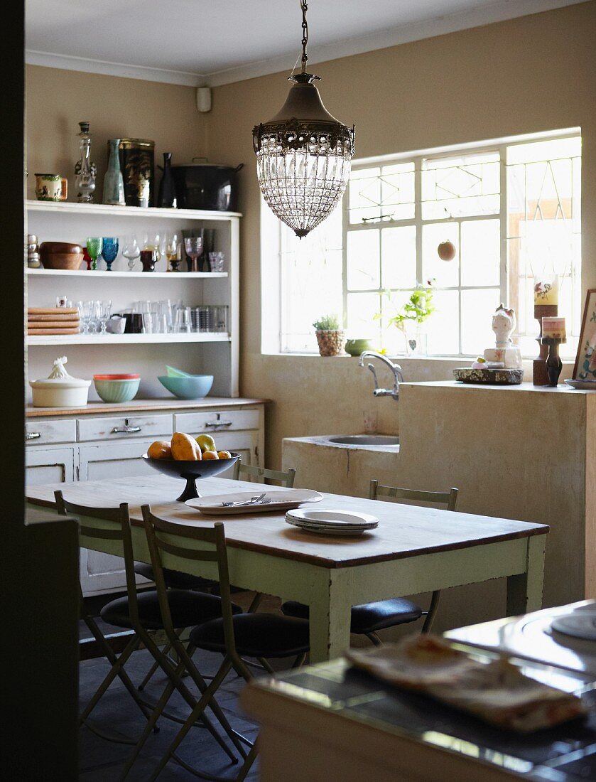 Simple kitchen with long wooden table, vintage-look dresser and masonry sink unit below window