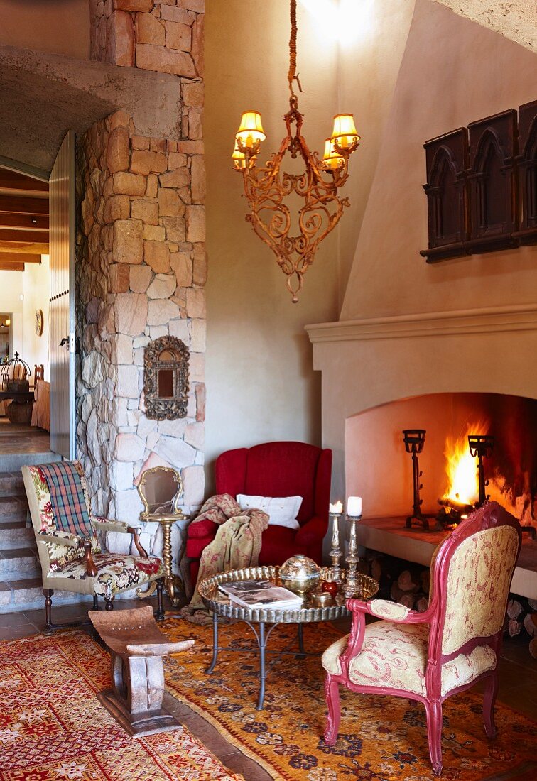 Various armchairs in cosy seating area next to open fire and doorway with stone column