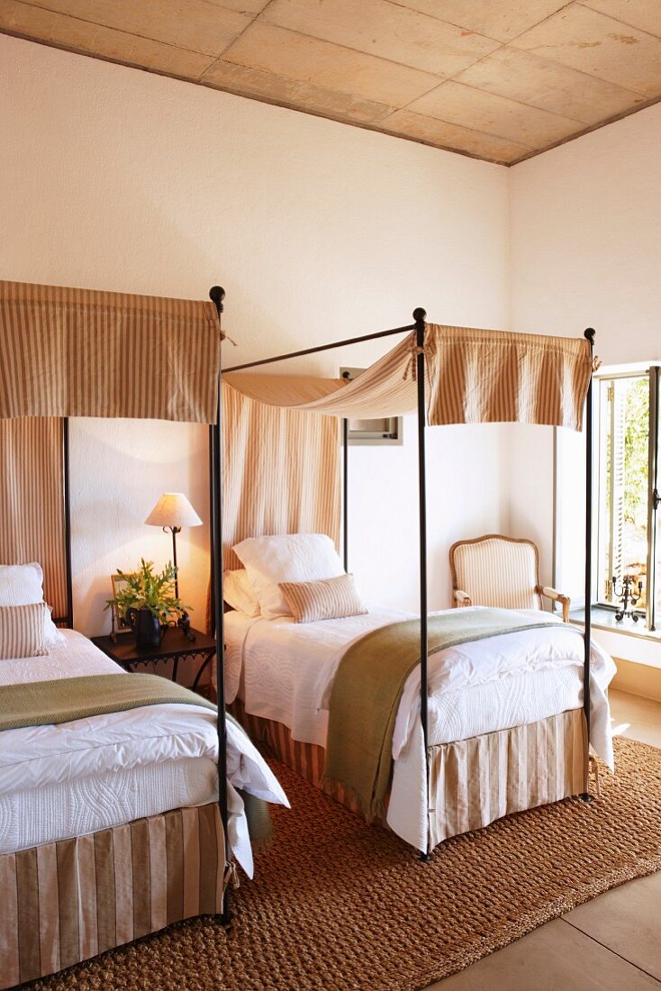 Twin beds with metal frames and canopies on seagrass rug in modern setting with exposed concrete ceiling