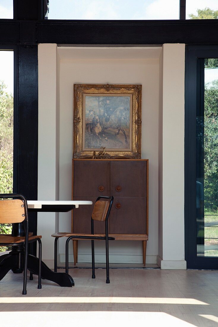 Retro table and chairs in front of cabinet on legs against wall between French windows