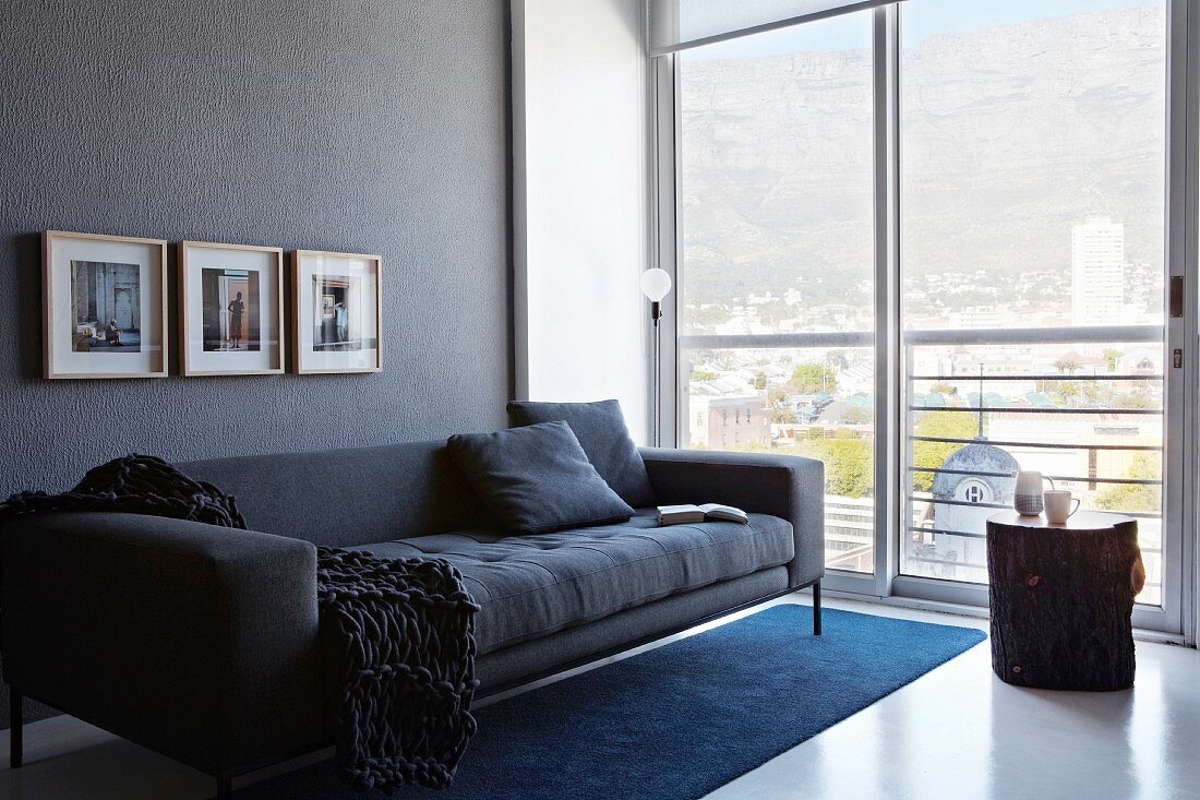 Modern, anthracite couch against grey wall next to glass wall with wonderful view of cityscape and mountains