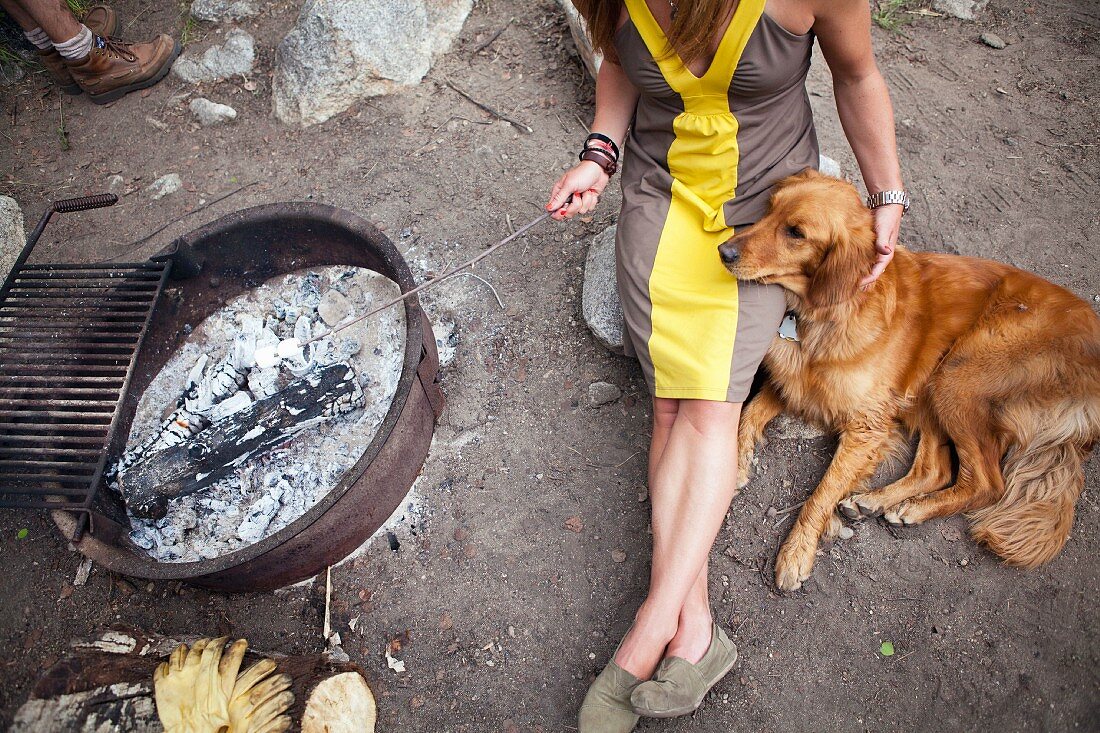 A Woman and Dog sitting by a Campfire Roasting Marshmallows