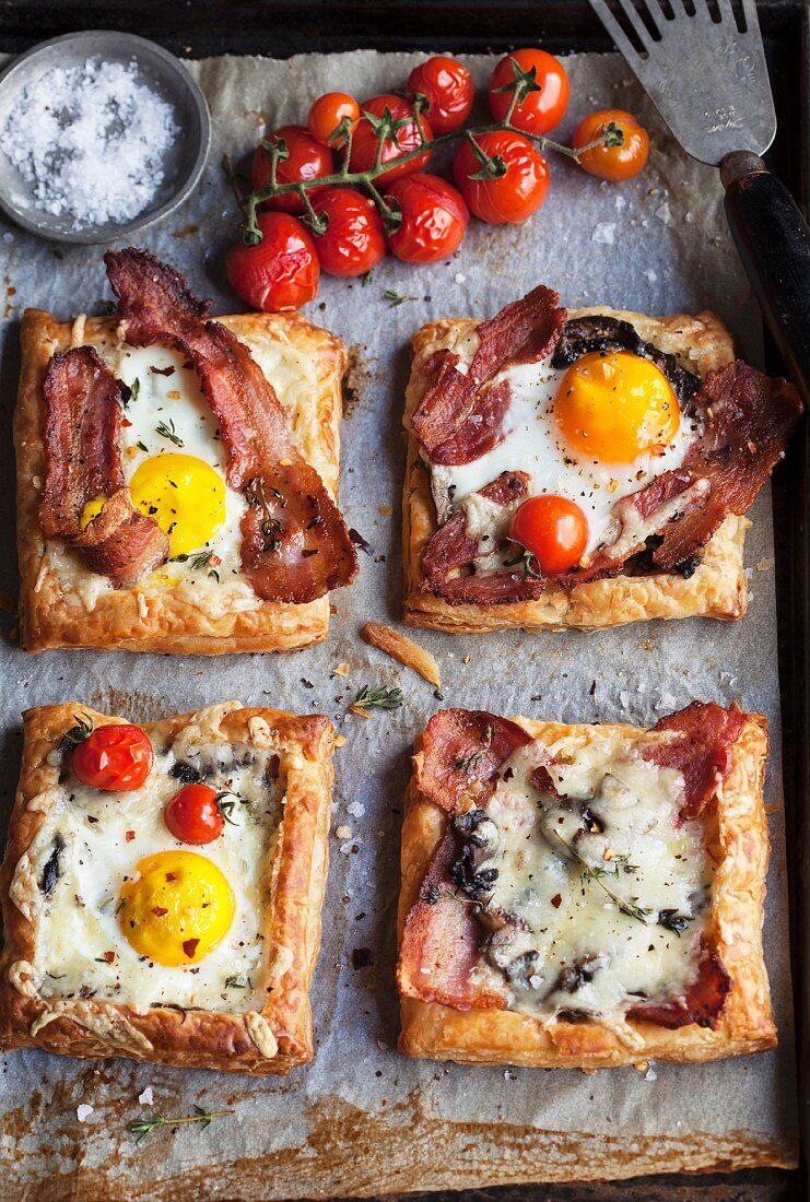 Puff pastry slices topped with bacon, fried egg, tomatoes and cheese