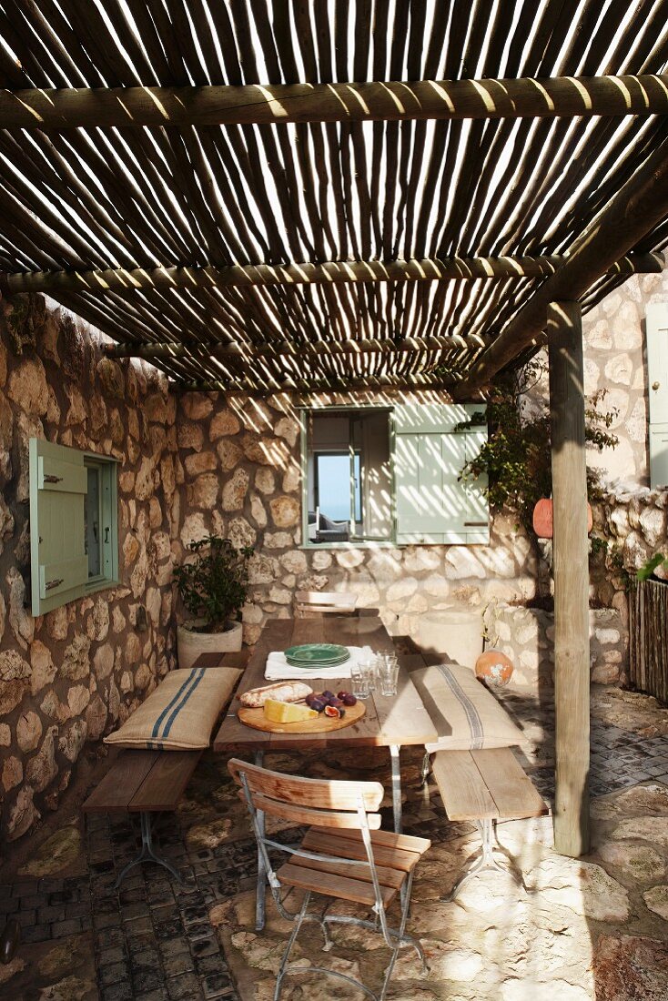 Rustikale Terrasse mit einfachem Sonnenschutz aus langen Bambusstangen und einem Natursteinboden