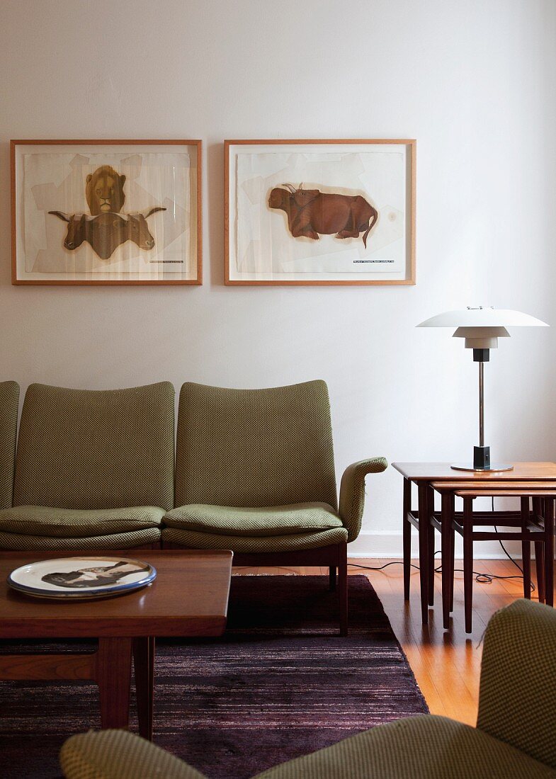 Wooden coffee table in front of upholstered bench below framed pictures on wall and classic table lamp on nested side tables