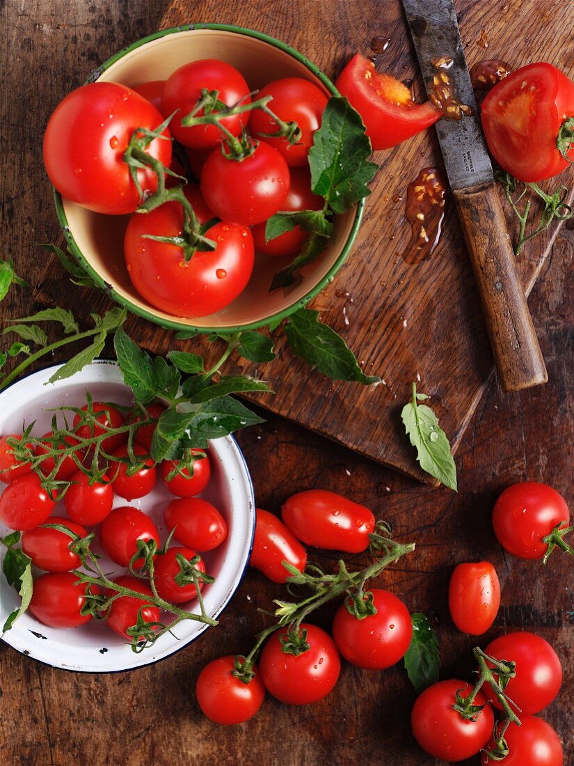 Assorted ripe tomatoes in bowls and on a wooden board