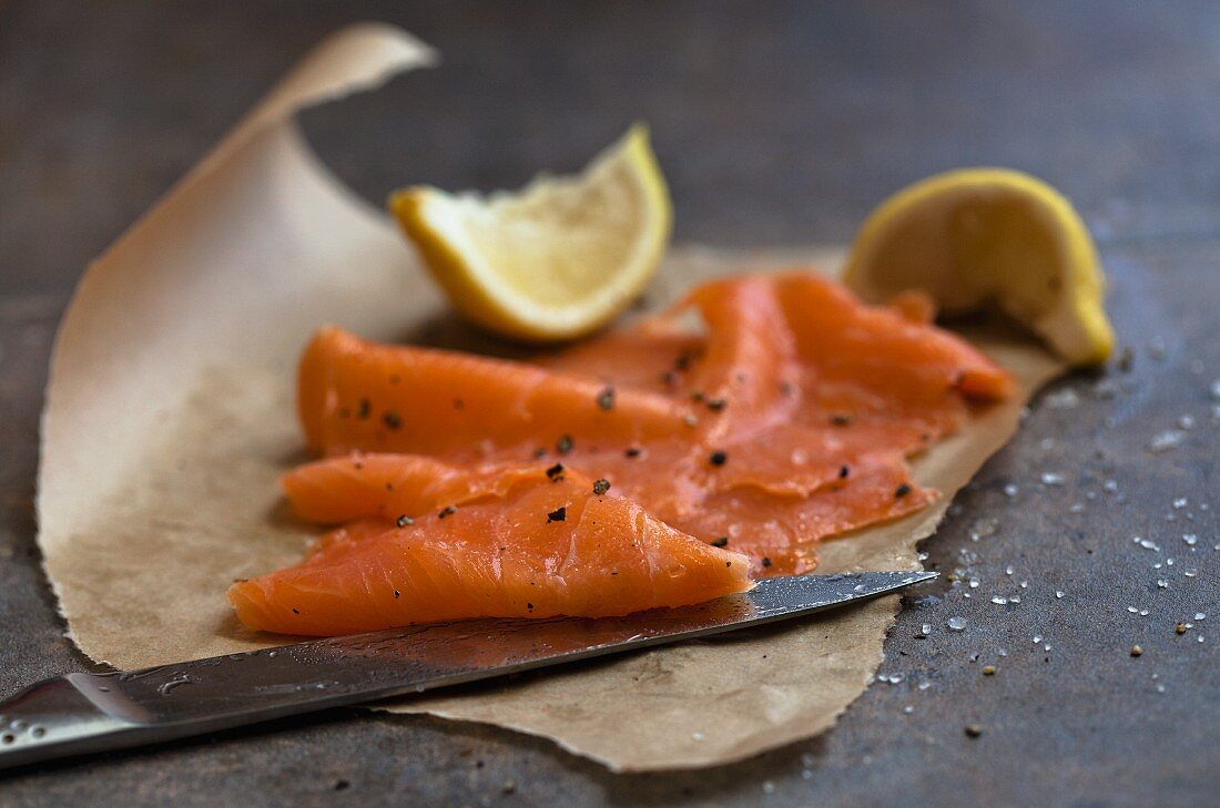 Smoked salmon, lemon wedges and a knife, on grease-proof paper