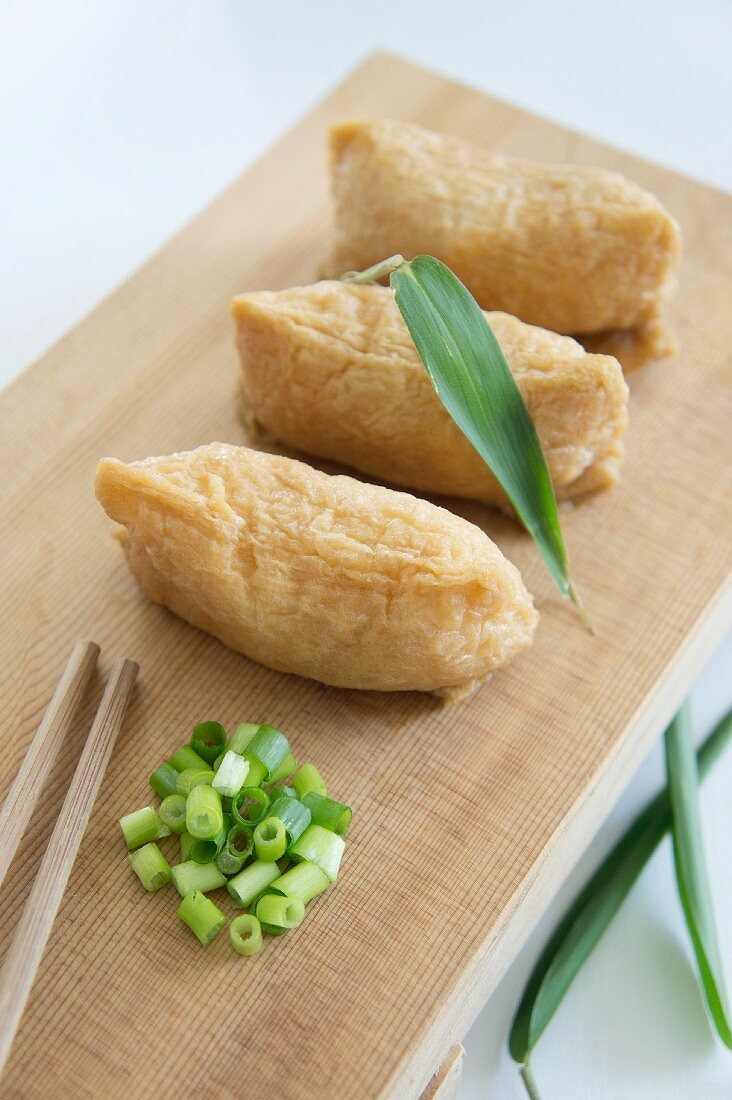 Inari sushi (rice encased in deep-fried tofu) with spring onions (negi) on a wooden slab