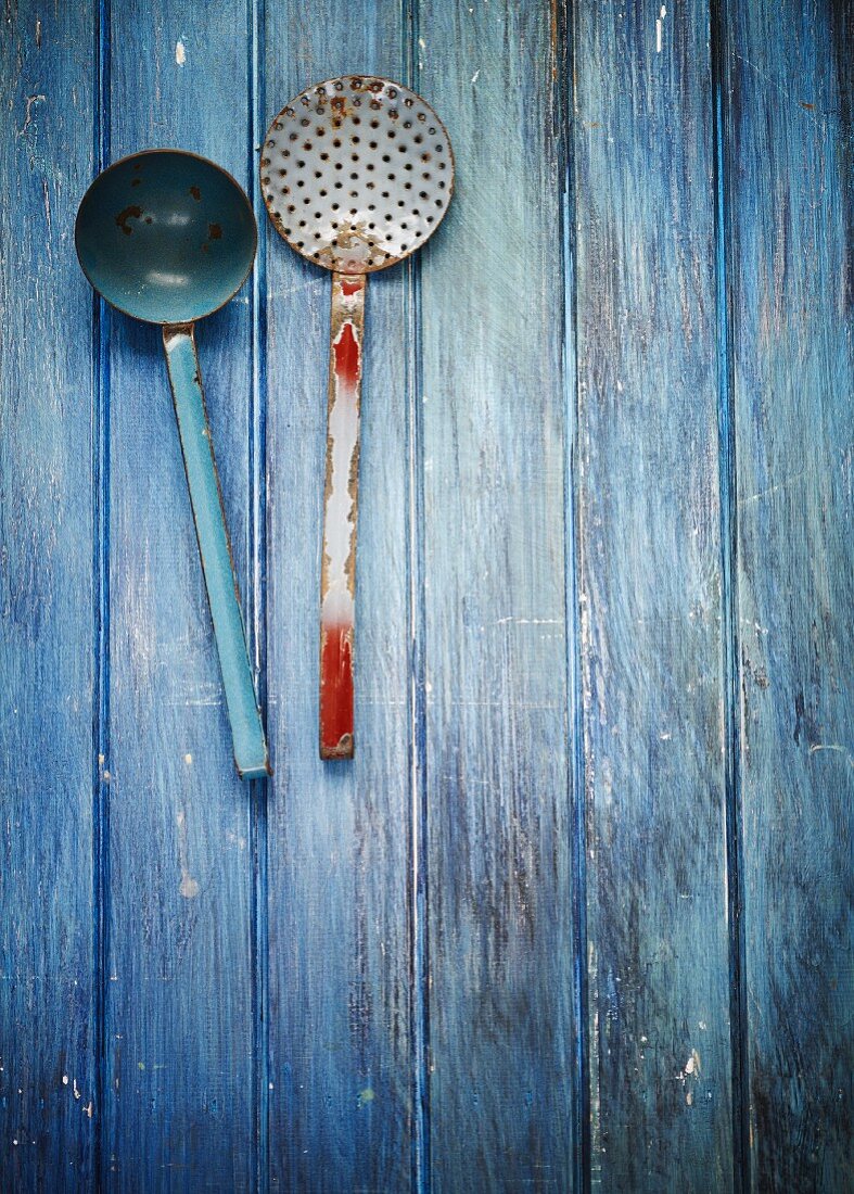 Alte Küchenutensilien (Kelle, Sieblöffel) auf blauem Holzuntergrund