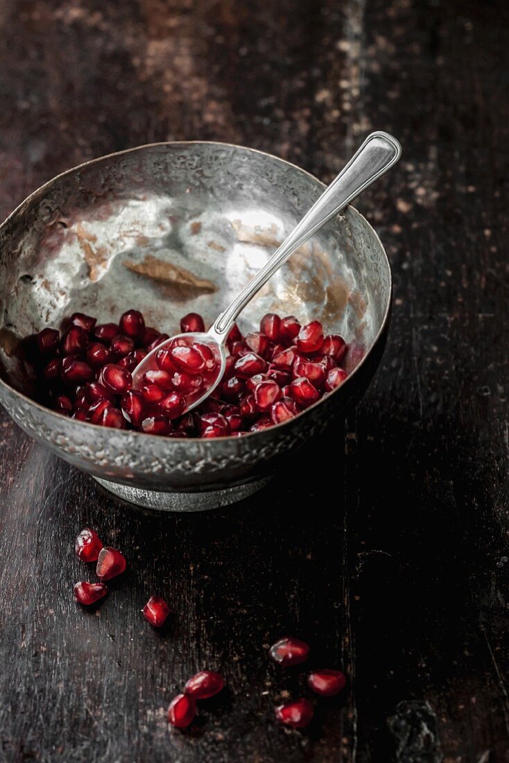 Pomegranate seeds in a metal bowl with a spoon