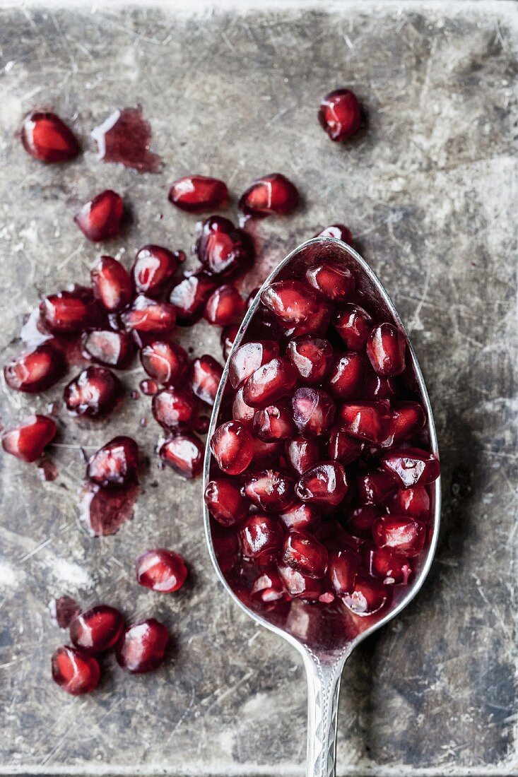 Pomegranate seeds and a spoon on a stone surface