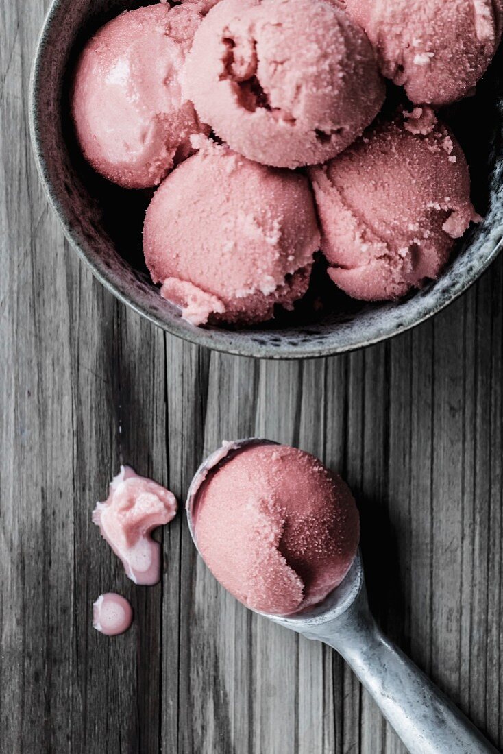 Several scoops of pomegranate ice cream in a bowl and an ice cream scoop