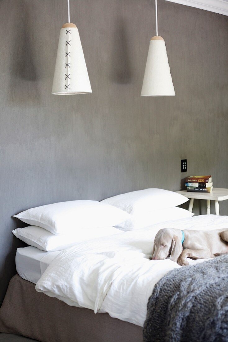 Cone-shaped pendant lamps above simple double bed against grey wall; dog asleep on bed