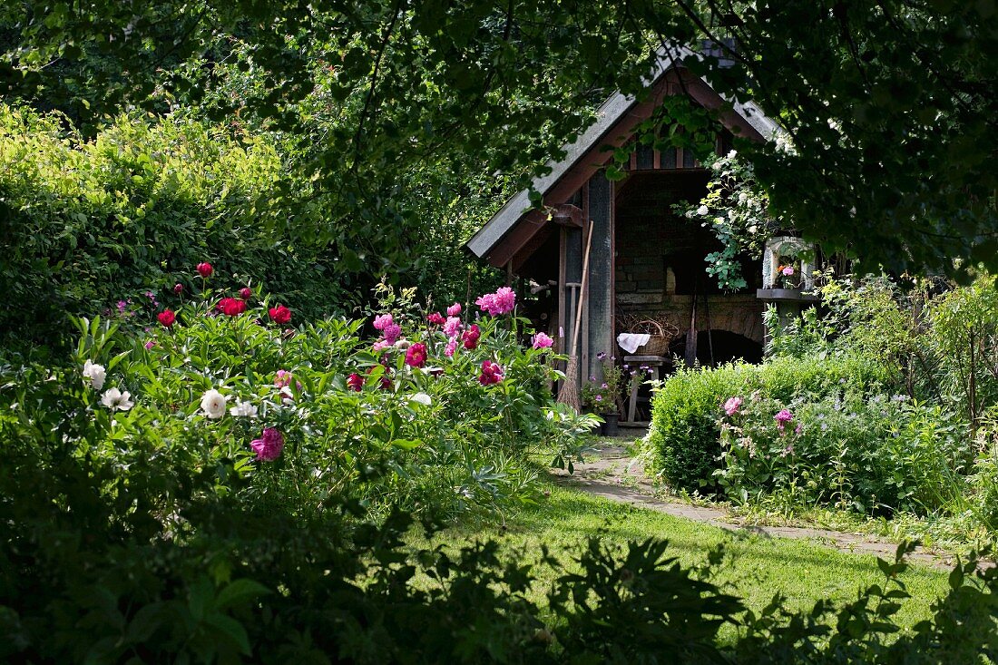 Sommerlicher Garten mit Blumen, im Hintergrund kleines Brotbackhaus aus Holz