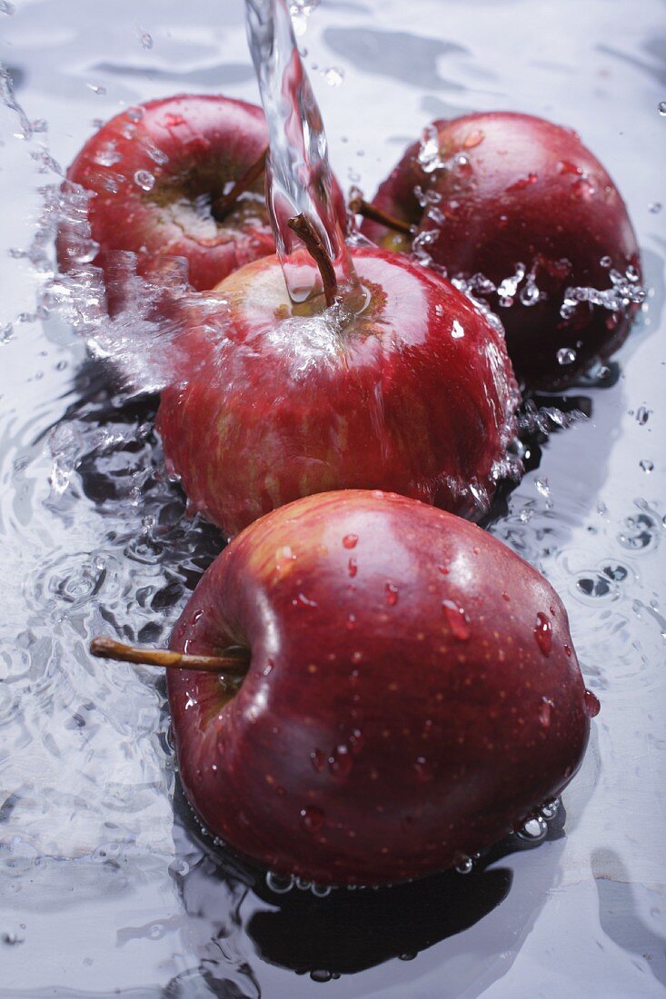 Red apples in water with a jet of water